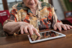 Un personnne âgée qui tape sur une tablette.